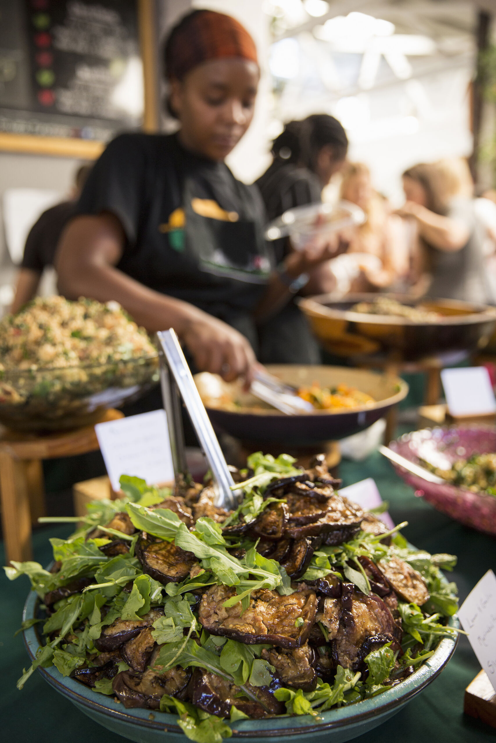 Stall holder serving eggplant salad at cooperative food market stall