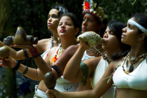 People holding a conch shell, carved object, and percussion instruments